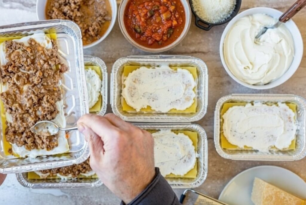 Mini lasagnas being assembled in small trays with layers of pasta, béchamel sauce, and meat filling.