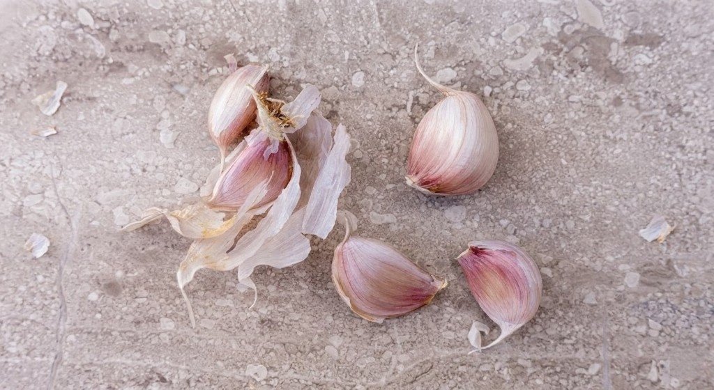 Several fresh garlic cloves, partly peeled, resting on a pale stone surface.