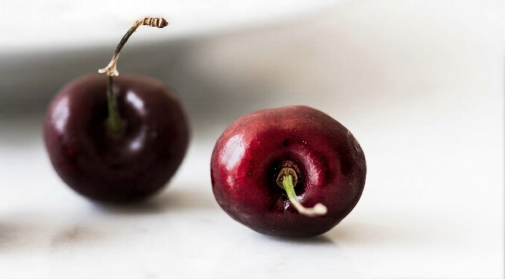Two dark red cherries on a light surface, one upright and one lying sideways, both glossy with stems attached.
