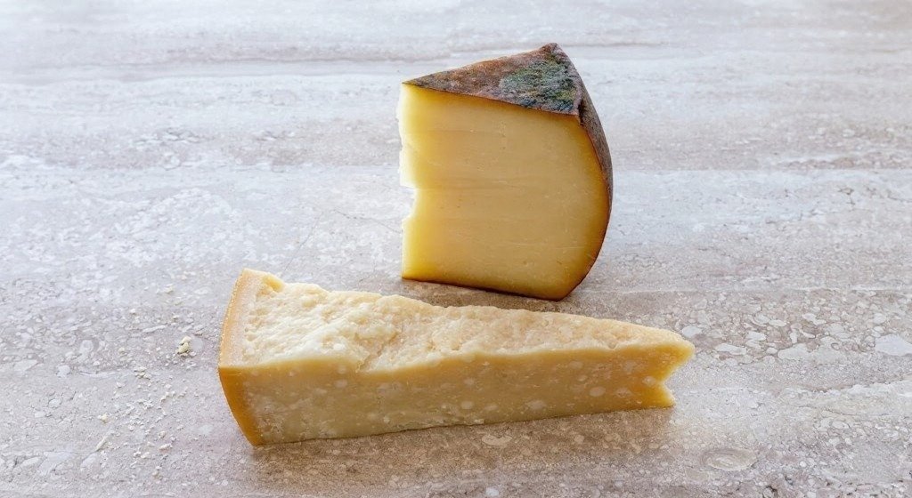 Two wedges of hard aged cheese on a pale stone surface.