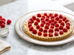 French Raspberry Tart Whole French raspberry tart with pastry cream on marble surface with fresh berries nearby.