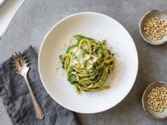 Make Trenette Al Pesto in an Easy Way Bowl of trenette al pesto topped with grated Parmigiano, pine nuts, and basil on a gray table.